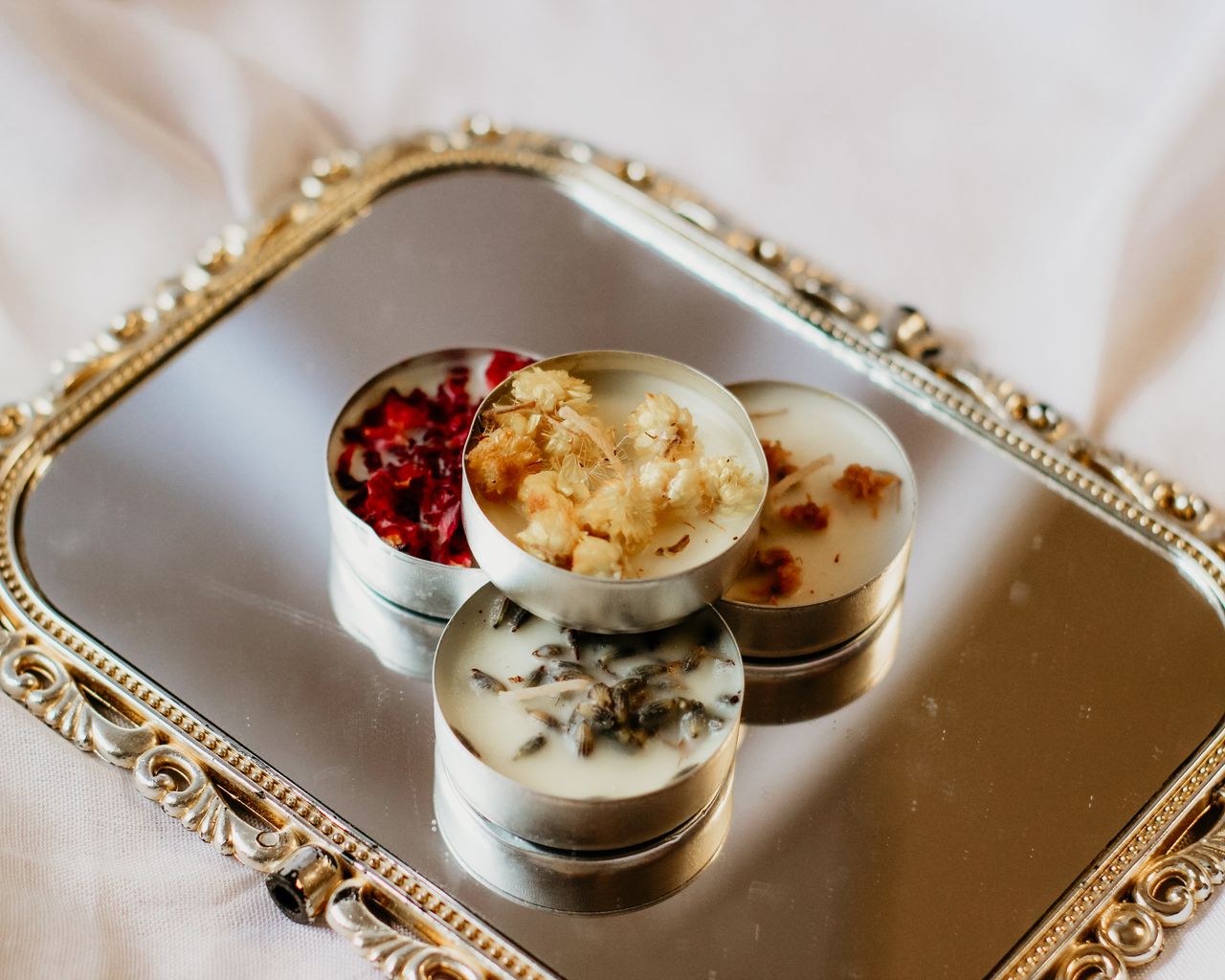 about-me-01 Aesthetic display of scented candles with dried flowers on a decorative mirrored tray.