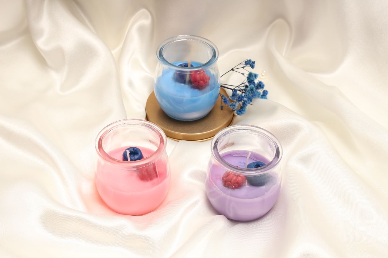 Three colorful scented candles on a luxurious satin fabric, creating a serene atmosphere.