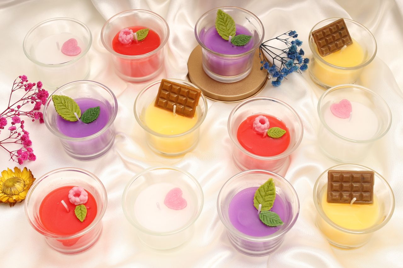 our-journey-01 Variety of colorful scented candles adorned with flowers and chocolate toppings on satin.