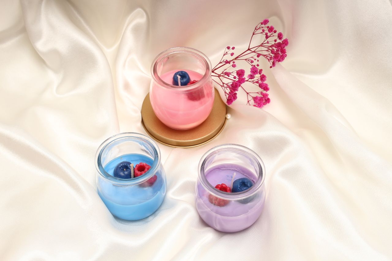 hero-img Three colorful scented candles with wax berries on satin fabric.